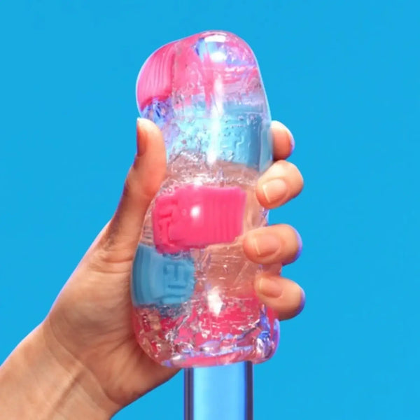 A hand holding TENGA BOBBLE CRAZY CUBES with pink and blue internal parts