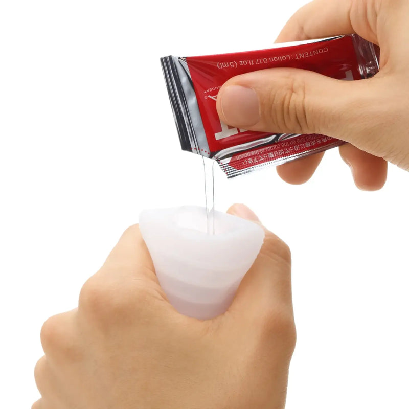 Hand squeezing POCKET TENGA COLD SPARK sex toy with liquid from a red packet